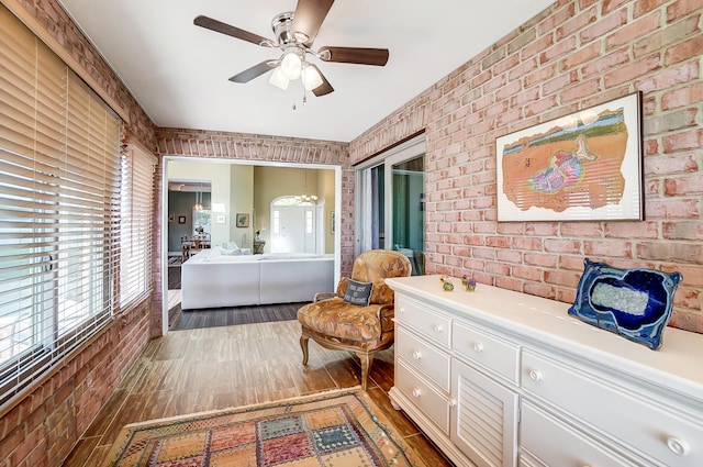 living area with dark wood-type flooring, ceiling fan, and brick wall