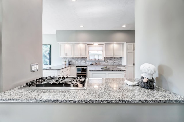 kitchen featuring white cabinetry, light stone counters, stainless steel gas stovetop, and wine cooler