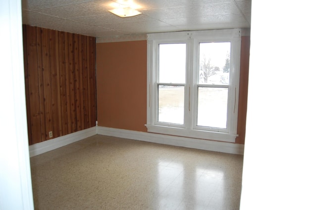 unfurnished room featuring baseboards, a wealth of natural light, and wooden walls