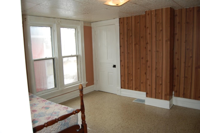 unfurnished bedroom with baseboards, visible vents, wooden walls, and a drop ceiling