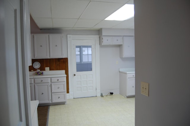 kitchen featuring light floors, white cabinets, a drop ceiling, and light countertops