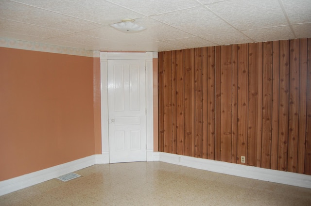 unfurnished room featuring a paneled ceiling, visible vents, wood walls, and baseboards