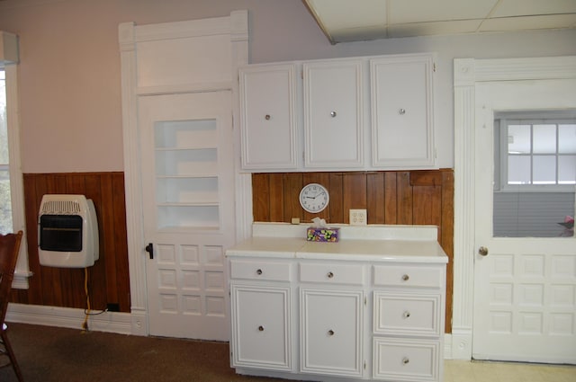 kitchen featuring wooden walls, light countertops, white cabinetry, and heating unit