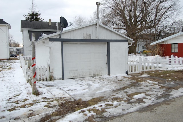 snow covered garage featuring a garage and fence