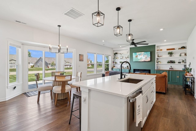 8202 Cherry Birch Dr, Tipp City, OH 45371 - kitchen with dark wood-style floors, a ceiling fan, a glass covered fireplace, an island with sink, and decorative light fixtures