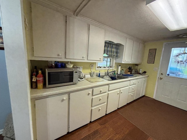 kitchen with dark wood-style flooring, light countertops, a textured ceiling, white cabinets, and a sink