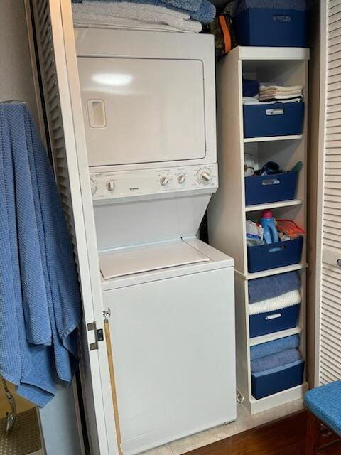 laundry area with stacked washer / drying machine, wood finished floors, and laundry area