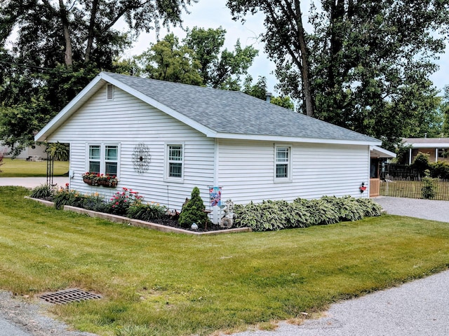 view of side of home featuring roof with shingles, fence, and a yard