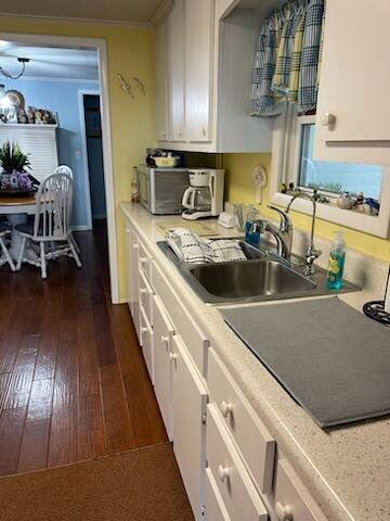 kitchen with a sink, light countertops, white cabinetry, and dark wood-type flooring