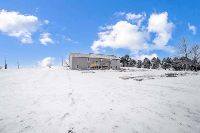 snow covered rear of property with a detached garage and a wooden deck