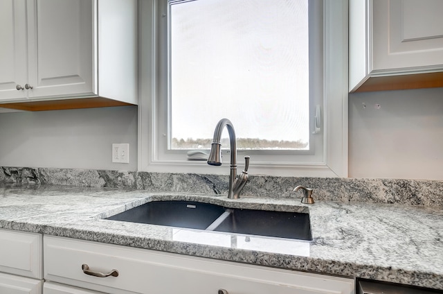 interior details featuring white cabinets, a sink, and light stone countertops