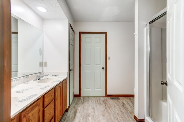 bathroom with baseboards, visible vents, wood finished floors, an enclosed shower, and vanity