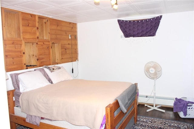 bedroom featuring wooden walls, dark hardwood / wood-style floors, and a baseboard heating unit