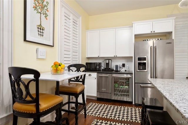 kitchen with white cabinets, stainless steel appliances, beverage cooler, light stone countertops, and dark wood-type flooring