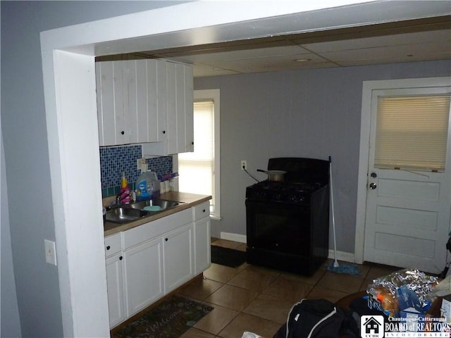 kitchen featuring white cabinetry, backsplash, black gas range oven, sink, and light tile flooring