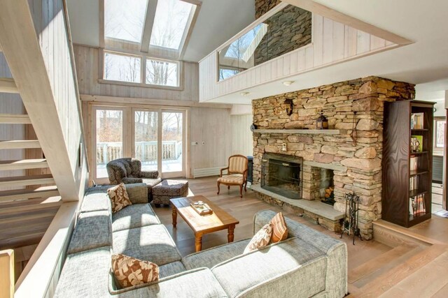 living room with high vaulted ceiling, a stone fireplace, a skylight, and light hardwood / wood-style flooring