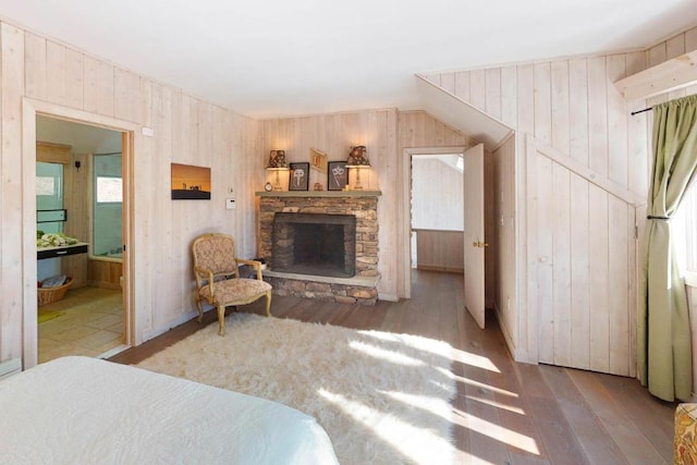 bedroom with wood walls, a stone fireplace, dark hardwood / wood-style floors, and ensuite bath