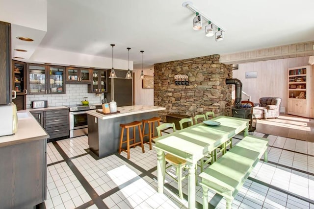 kitchen featuring a wood stove, stainless steel range with electric stovetop, backsplash, decorative light fixtures, and dark brown cabinetry