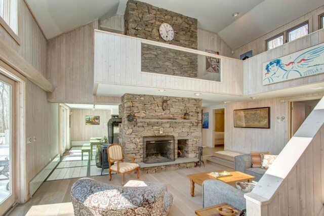 living room featuring a stone fireplace, wooden walls, and high vaulted ceiling