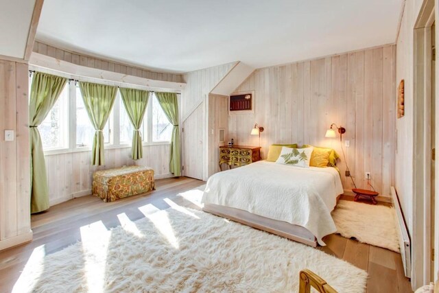 bedroom featuring wooden walls, light wood-type flooring, and a baseboard heating unit