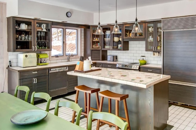 kitchen with a kitchen bar, dishwashing machine, tasteful backsplash, built in fridge, and tile counters