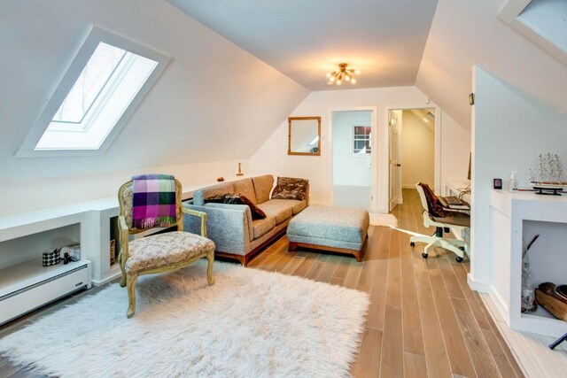 sitting room with vaulted ceiling with skylight, baseboard heating, and light hardwood / wood-style floors