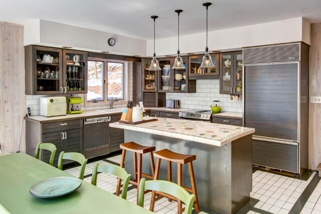 kitchen with built in fridge, tile counters, tasteful backsplash, a breakfast bar area, and dishwasher