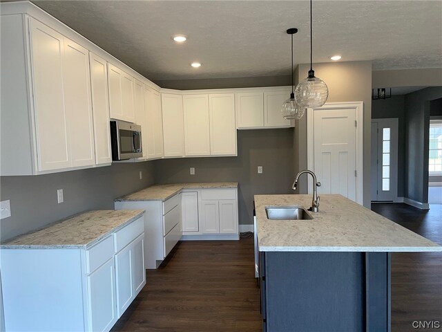 kitchen with white cabinetry, dark hardwood / wood-style floors, sink, an island with sink, and pendant lighting