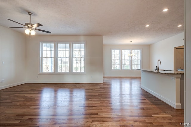 unfurnished living room with a textured ceiling, dark hardwood / wood-style flooring, a healthy amount of sunlight, and ceiling fan with notable chandelier