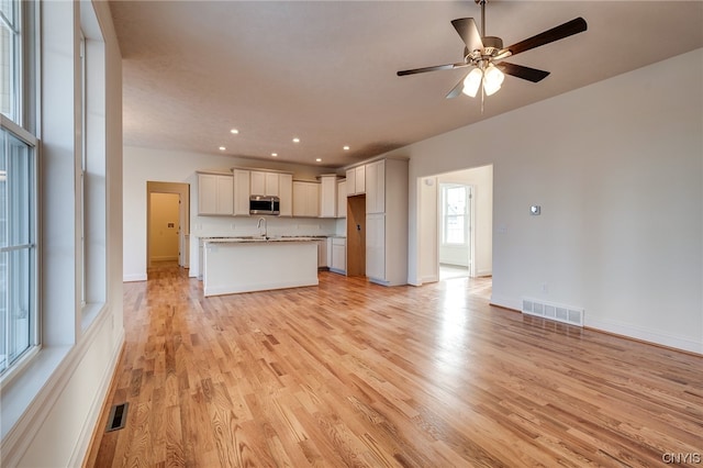 unfurnished living room featuring ceiling fan, sink, and light wood-type flooring