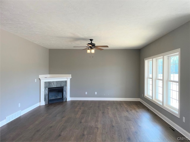 unfurnished living room featuring ceiling fan, a textured ceiling, dark wood-type flooring, and a tiled fireplace