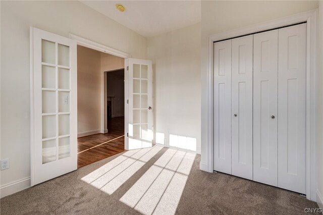 unfurnished bedroom featuring french doors, a closet, and dark carpet