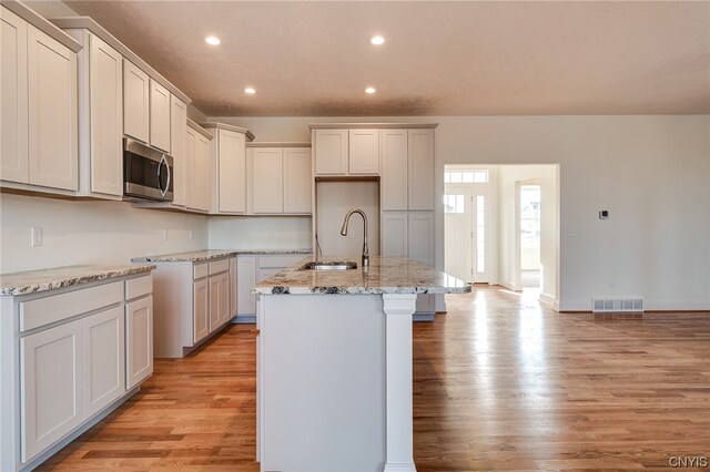 kitchen with light hardwood / wood-style flooring, light stone countertops, sink, and an island with sink