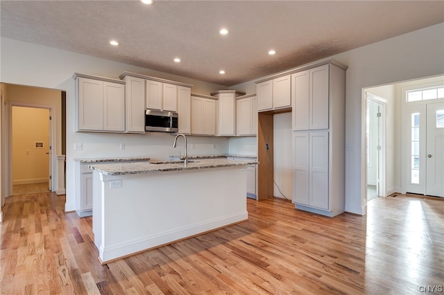 kitchen featuring an island with sink, light hardwood / wood-style floors, sink, and light stone counters