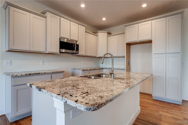 kitchen with light hardwood / wood-style flooring, an island with sink, and light stone countertops