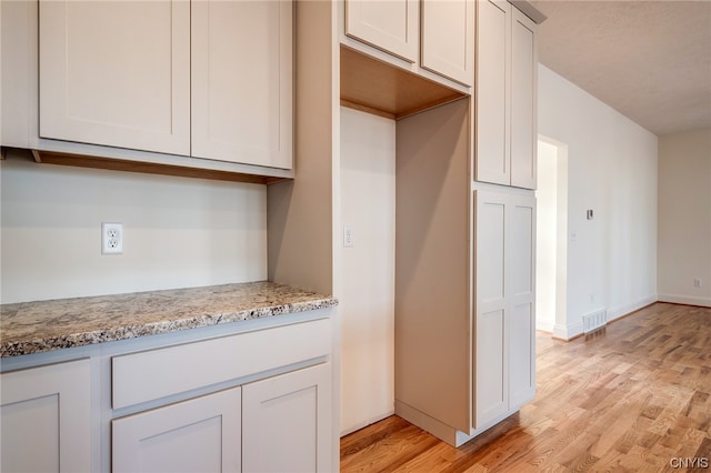 kitchen featuring light stone counters, white cabinetry, and light hardwood / wood-style flooring