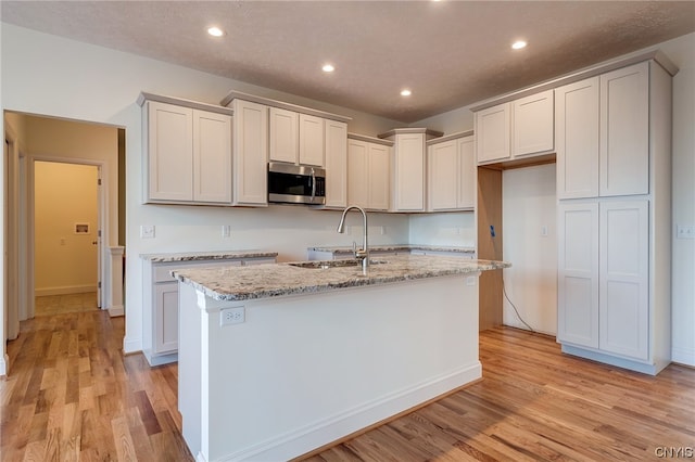 kitchen featuring light stone counters, a kitchen island with sink, sink, and light hardwood / wood-style flooring