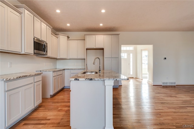 kitchen featuring light stone countertops, light hardwood / wood-style flooring, sink, and an island with sink