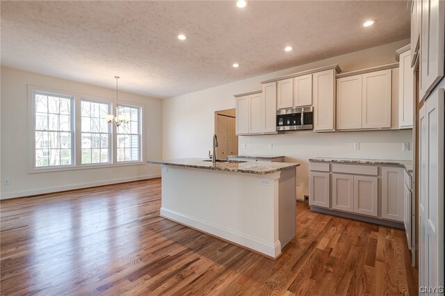 kitchen with a kitchen island with sink, sink, hanging light fixtures, dark wood-type flooring, and a notable chandelier