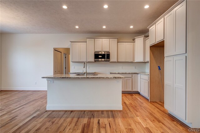 kitchen featuring light hardwood / wood-style floors, a kitchen island with sink, white cabinets, and light stone countertops