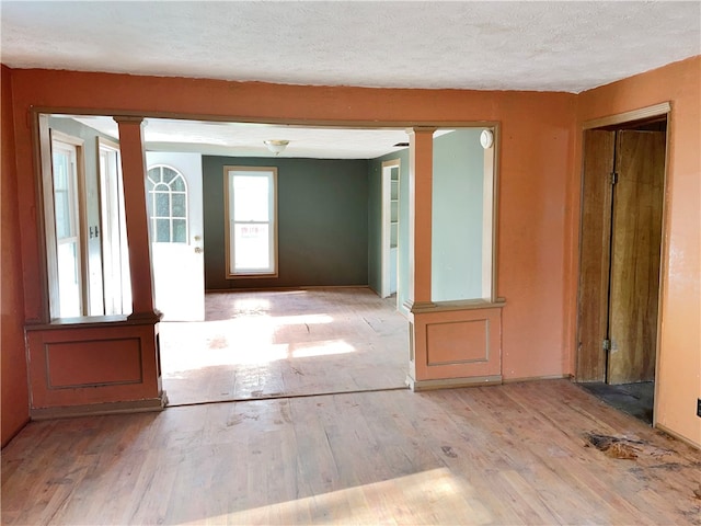 spare room with a textured ceiling, ornate columns, and light hardwood / wood-style flooring