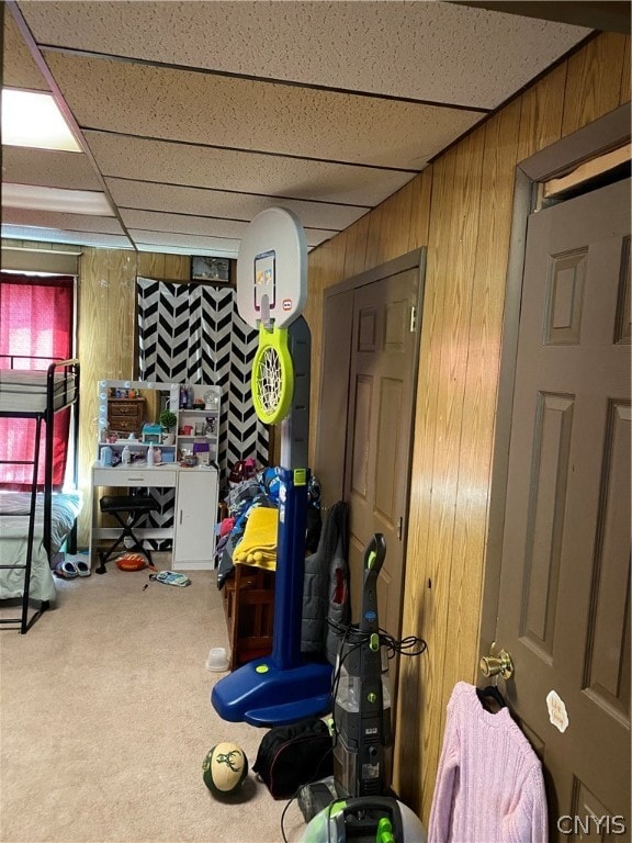 playroom featuring carpet flooring, wood walls, and a drop ceiling