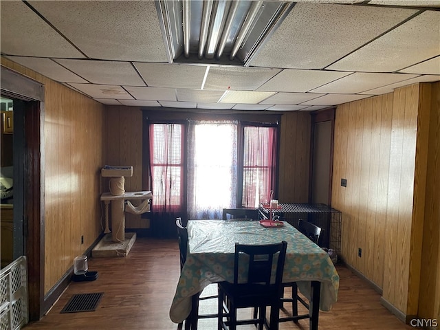 dining area with a drop ceiling, wood walls, and dark hardwood / wood-style floors