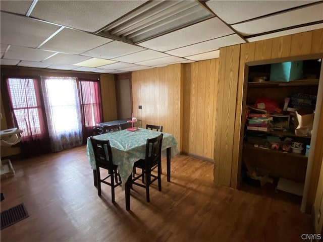 dining space with a paneled ceiling, wood walls, wood finished floors, and visible vents