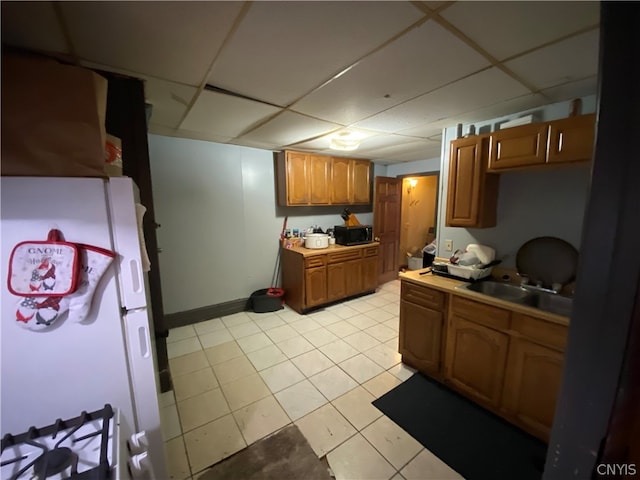 kitchen featuring white refrigerator, a paneled ceiling, light tile patterned flooring, and sink