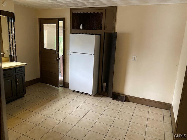 kitchen with dark brown cabinets, light tile patterned floors, and white fridge