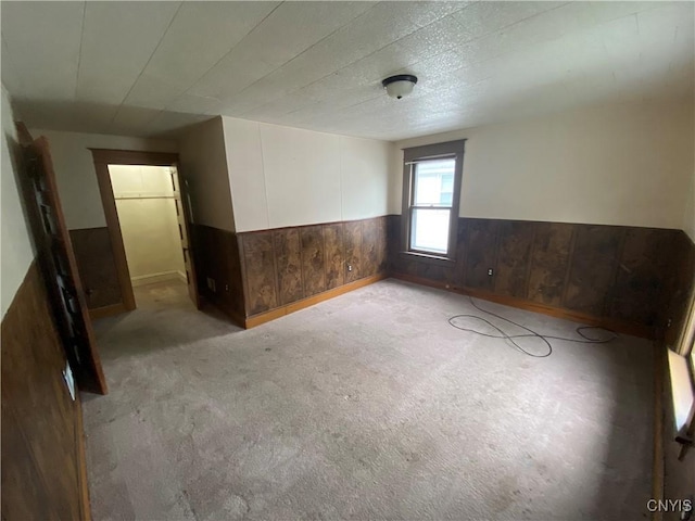 carpeted empty room with a wainscoted wall and wood walls