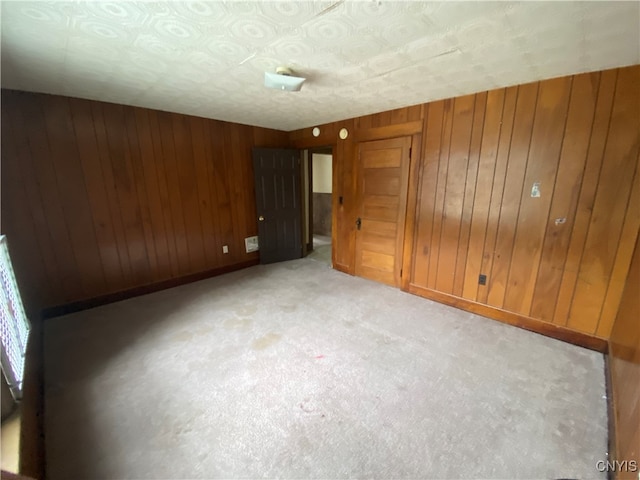 unfurnished bedroom featuring light carpet, a textured ceiling, and wood walls