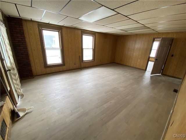 spare room with light wood finished floors, visible vents, a drop ceiling, and wood walls