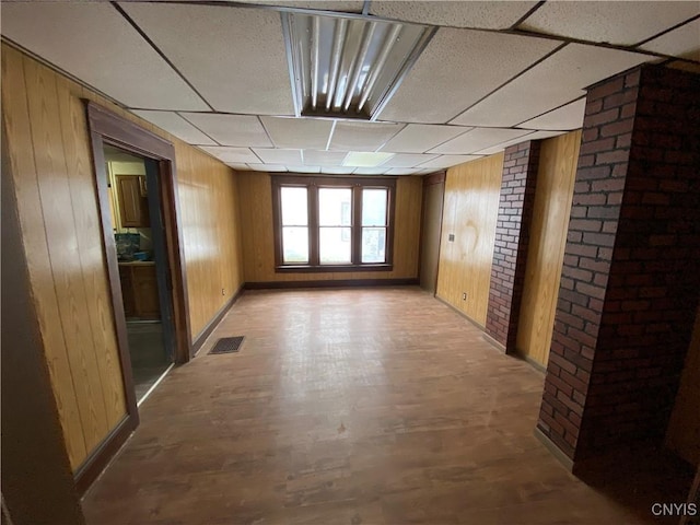 empty room featuring brick wall, a paneled ceiling, visible vents, and wooden walls